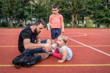 Baba kızına spor sahasında su veriyor.