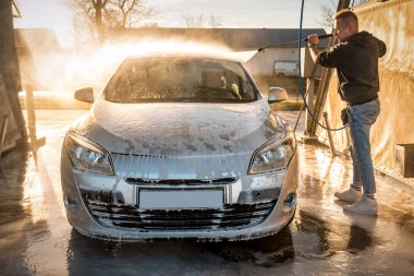 Adam gün batımında oto yıkamada pıhtıyı yıkıyor.