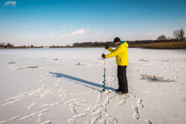 Sarı elbiseli balıkçı buzda bir delik açıyor.