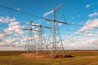 Mavi gökyüzünün altında yüksek voltajlı elektrik hatları var.