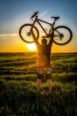 Sürücü, güzel bir günbatımı gökyüzüne karşı bisikletini muzaffer bir şekilde kaldırır. Spor ve eğlence teması