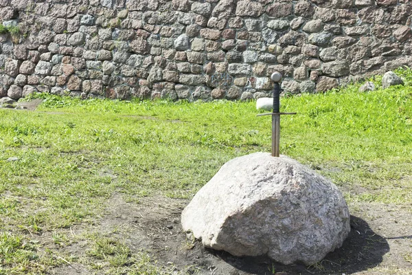 A sword in a stone on the background of a stone castle wall