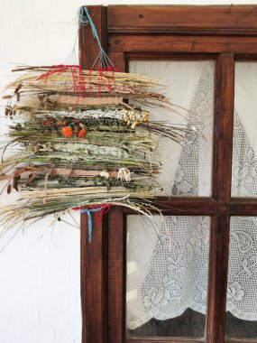 Kurumuş otların ve çiçeklerin hasır süslemesi bir köy evinin camında asılı.