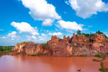Önünde kırmızı su, arkasında beyaz bulutlar olan taştan bir dağ manzarası.