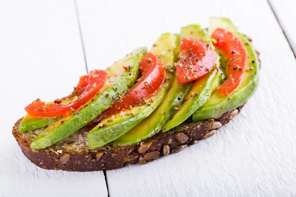 Sabroso sándwich de aguacate con tomate sobre pan de centeno oscuro . Imágenes de stock libres de derechos