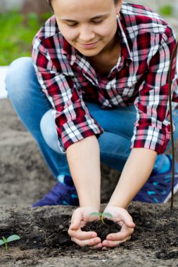 Kadın toprak ve genç bitki elinde tutuyor.