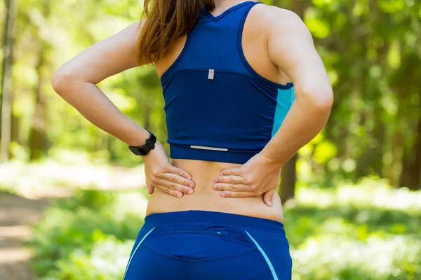 Dolor de espalda. Mujer joven en ropa deportiva azul con smartwatches frotar — Foto de Stock