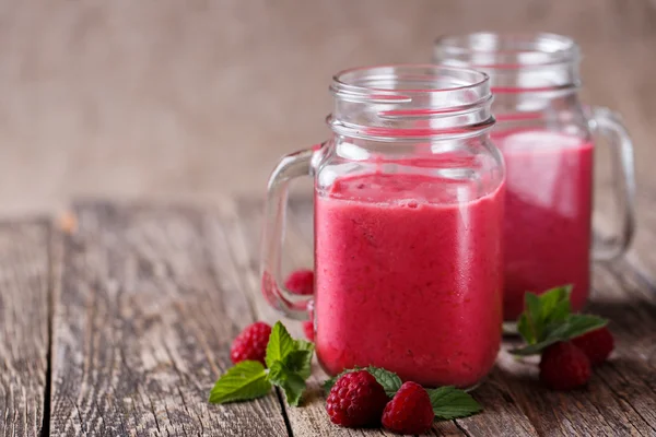 A fából készült asztal üvegedénybe ízletes málna smoothie. — Stock Fotó