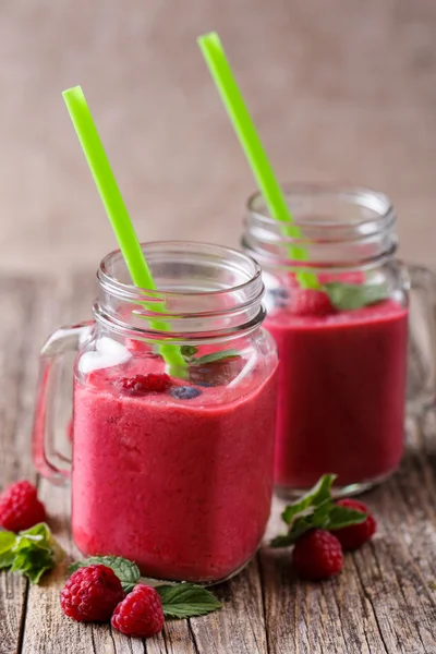 A fából készült asztal üvegedénybe ízletes málna smoothie. — Stock Fotó