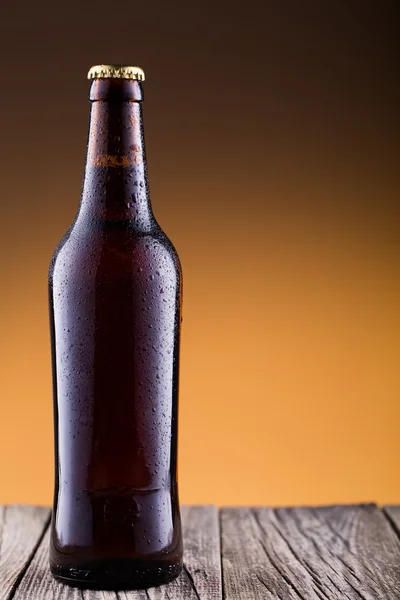 Beer bottle with water drops in golden background.
