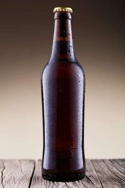 Beer bottle with water drops in brown background.