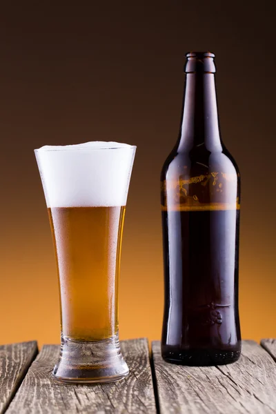 Beer bottle with a glass in golden background. — Stock Photo, Image