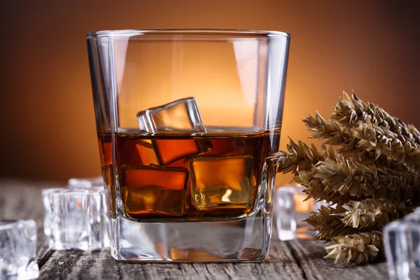 Un vaso de whisky con hielo y trigo sobre una mesa de madera . — Foto de Stock