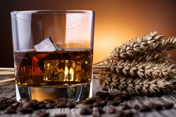 Glass of whiskey with ice and wheat on a wooden table. — Stock Photo, Image