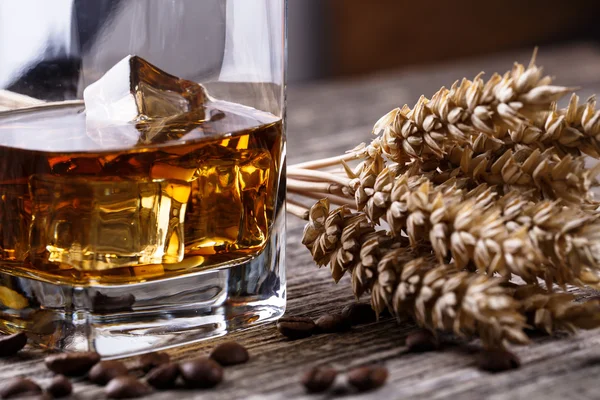 Un vaso de whisky con hielo y trigo sobre una mesa de madera . —  Fotos de Stock