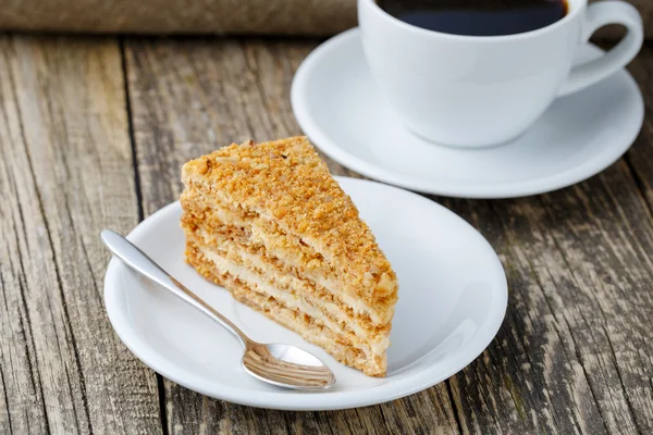 Tasty honey cake with cup of coffee on wooden background. — Stock Photo, Image