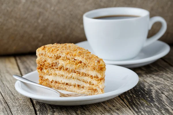 Sabroso pastel de miel con taza de café sobre fondo de madera . — Foto de Stock