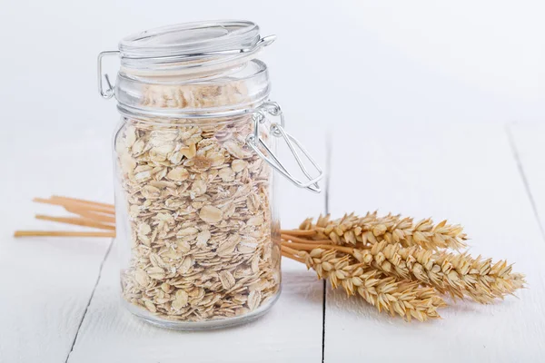 Los copos de avena en frasco de vidrio y trigo . — Foto de Stock