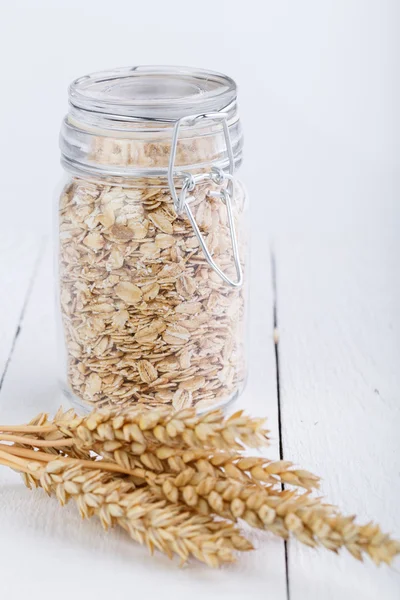 The oat flakes in glass jar and wheat. — Stock Photo, Image