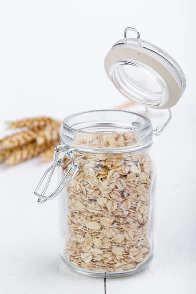 The oat flakes in glass jar and wheat. — Stock Photo, Image