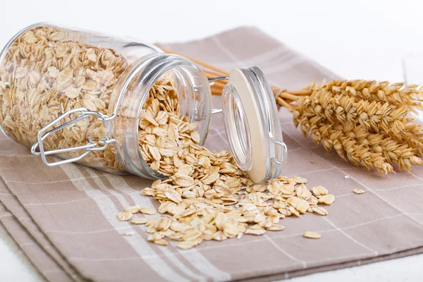 The oat flakes in glass jar and wheat. — Stock Photo, Image
