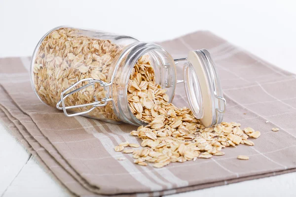 The oat flakes in glass jar on brown towel. — Stock Photo, Image