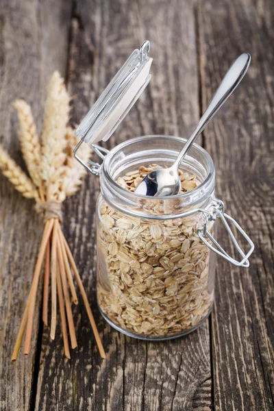 The oat flakes in jar and wheat on wooden table. — Stock Photo, Image