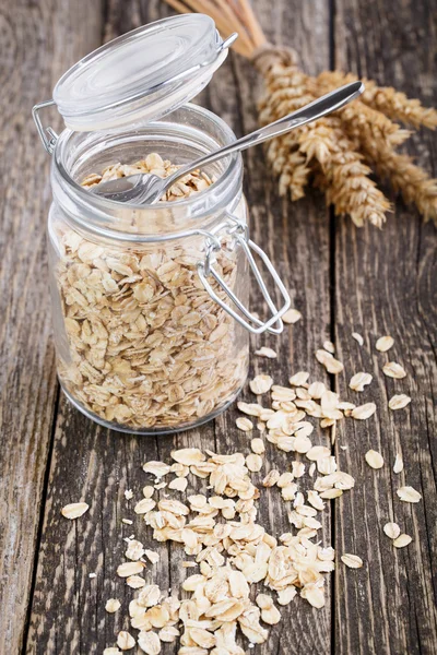 Oat flakes spilled out from jar and wheat. — Stock Photo, Image