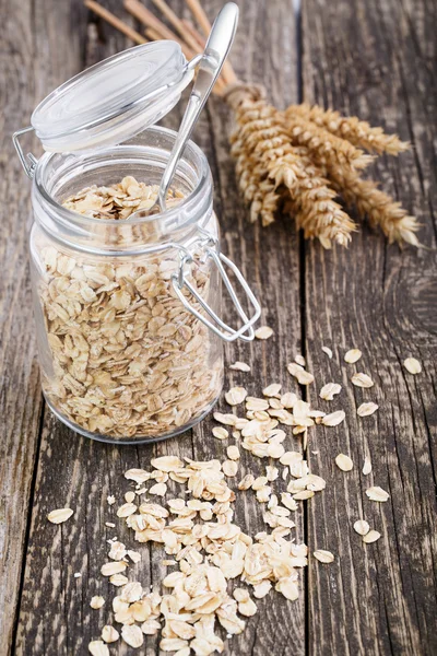 Oat flakes spilled out from jar and wheat. — Stock Photo, Image