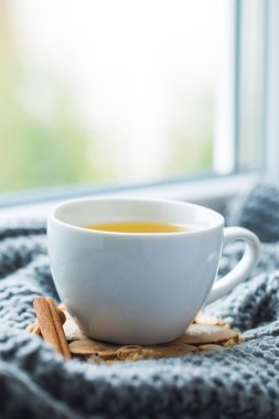 Beyaz papatya çayı pencere üzerinde gri eşarp ile fincan.