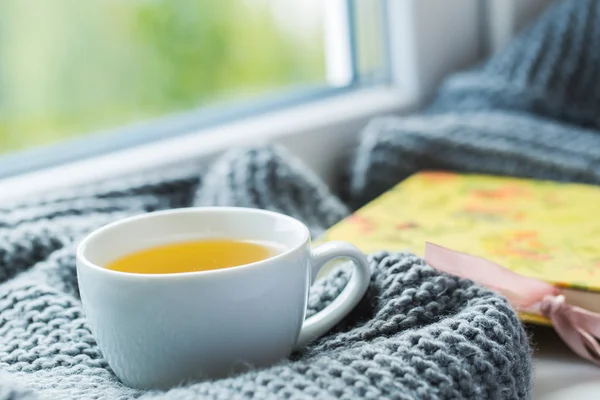 Weiße Tasse Kamillentee mit grauem Schal auf der Fensterbank. — Stockfoto