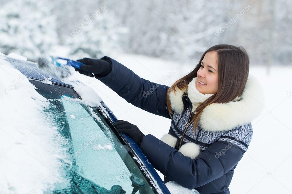 Beautiful young woman removing snow from her car.
