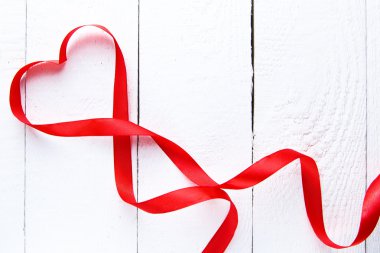Kalp şekli kırmızı kurdele beyaz masada.