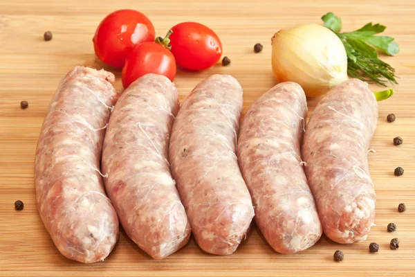 Uncooked sausage with vegetables on the chopping board — Stock Photo, Image