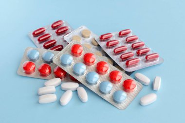 Çeşitli ilaç hapları, haplar ve kapsüller mavi arka planda.