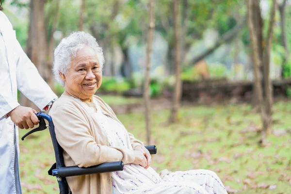 Doctor help and care Asian senior or elderly old lady woman patient sitting on wheelchair at park in nursing hospital ward, healthy strong medical concept.