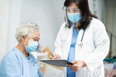 Doktor, enfeksiyon kapmasın diye hastanede yüz maskesi takan Asyalı yaşlı ya da yaşlı kadın hastaları kontrol etmek için steteskop kullanıyor..