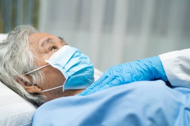 Doktor, enfeksiyon kapmasın diye hastanede yüz maskesi takan Asyalı yaşlı ya da yaşlı kadın hastaları kontrol etmek için steteskop kullanıyor..