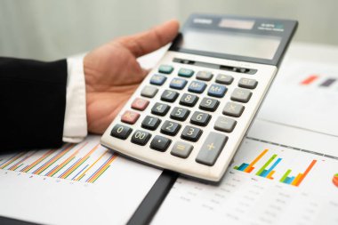 Modern ofis, finans ve iş konseptinde grafik grafik grafiği ve hesap makinesiyle çalışan ve finansal raporları analiz eden Asyalı muhasebeci.