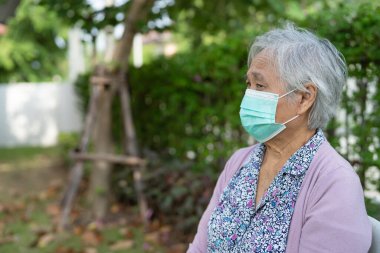 Güvenlik enfeksiyonu Covid-19 Coronavirus 'u korumak için parkta yeni bir maske takan Asyalı yaşlı ya da yaşlı kadın..