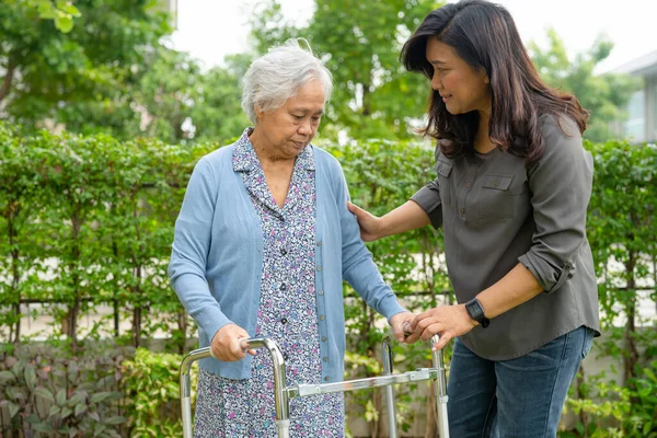 Help and care Asian senior or elderly old lady woman use walker with strong health while walking at park in happy fresh holiday.