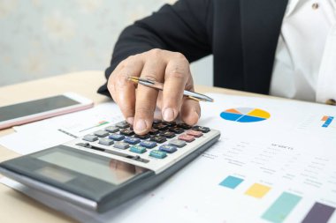 Modern ofis, finans ve iş konseptinde grafik grafik grafiği ve hesap makinesiyle çalışan ve finansal raporları analiz eden Asyalı muhasebeci.
