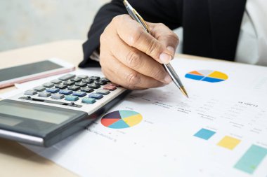 Modern ofis, finans ve iş konseptinde grafik grafik grafiği ve hesap makinesiyle çalışan ve finansal raporları analiz eden Asyalı muhasebeci.