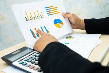 Modern ofis, finans ve iş konseptinde grafik grafik grafiği ve hesap makinesiyle çalışan ve finansal raporları analiz eden Asyalı muhasebeci.
