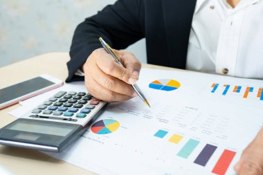 Modern ofis, finans ve iş konseptinde grafik grafik grafiği ve hesap makinesiyle çalışan ve finansal raporları analiz eden Asyalı muhasebeci.
