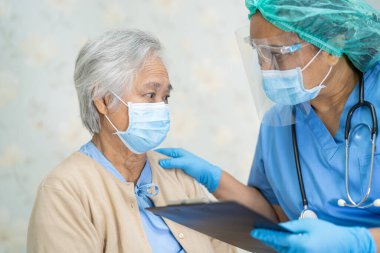 Doktor, enfeksiyon kapmasın diye hastanede yüz maskesi takan Asyalı yaşlı ya da yaşlı kadın hastaları kontrol etmek için steteskop kullanıyor..