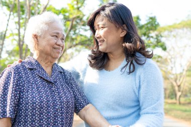 Asya 'lı yaşlı ve yaşlı kadınlara yardım ve yataklık etmek için parkta yürürken sağlıklı bir şekilde yürüyen yaşlı kadın kullanılıyor..