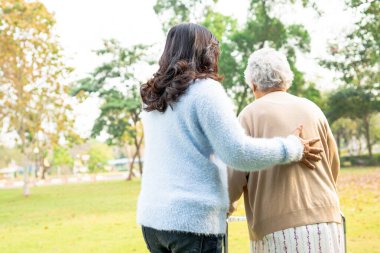 Asya 'lı yaşlı ve yaşlı kadınlara yardım ve yataklık etmek için parkta yürürken sağlıklı bir şekilde yürüyen yaşlı kadın kullanılıyor.. 