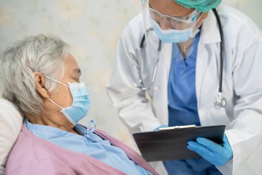 Doktor, enfeksiyon kapmasın diye hastanede yüz maskesi takan Asyalı yaşlı ya da yaşlı kadın hastaları kontrol etmek için steteskop kullanıyor..