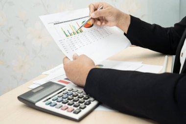 Modern ofis, finans ve iş konseptinde grafik grafik grafiği ve hesap makinesiyle çalışan ve finansal raporları analiz eden Asyalı muhasebeci.